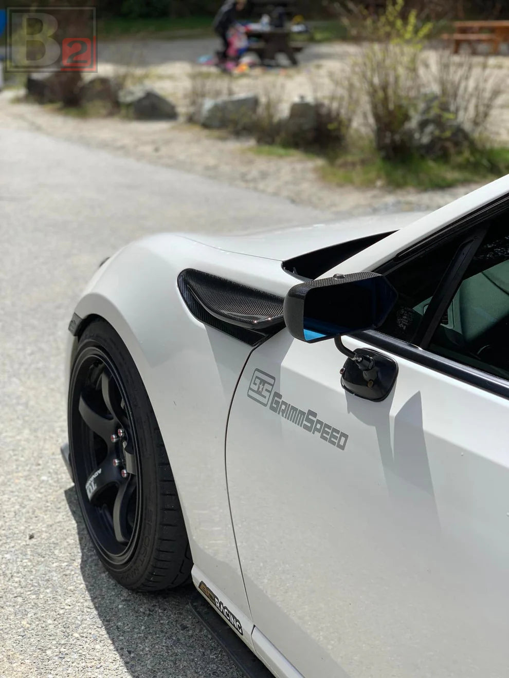 A white sports car with black wheels and a pair of Box 2 Formula side mirrors attached to the car's doors.